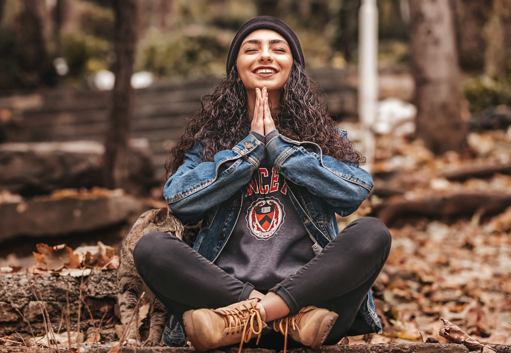 A young woman with dark brown, curly hair, smiling with her hands in prayer, sitting on the ground