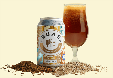 a can of kvass with a full glass of kvass in the background and grains scattered around
