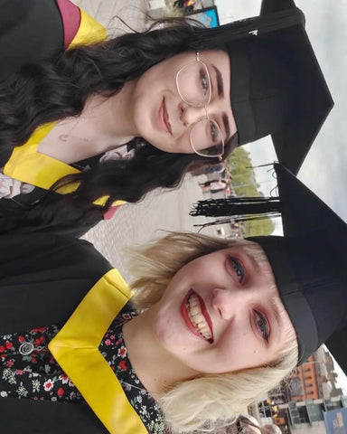 myself and a friend smiling for a photo in our graduation gowns, graduating from Textiles at Cardiff Met in Cardiff Bay
