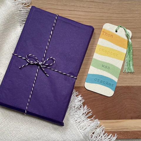 A picture of a book, wrapped in purple tissue paper, alongside a colourful bright bookmark