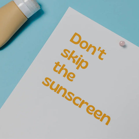 A flatlay image which shows a memo pad with the words 'Don't forget the sunscreen' typed in yellow print