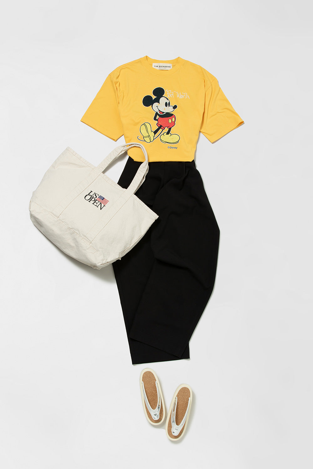 ザ シンゾーンのミッキーマウスプリントの黄色いTシャツとクラネの黒いパンツにシンゾーンのトートを合わせたスタイリング