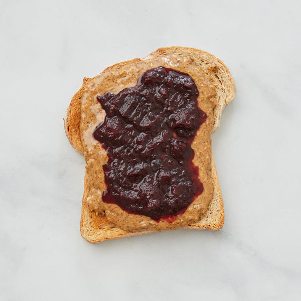 Almond butter and jam on toast on a white marble background