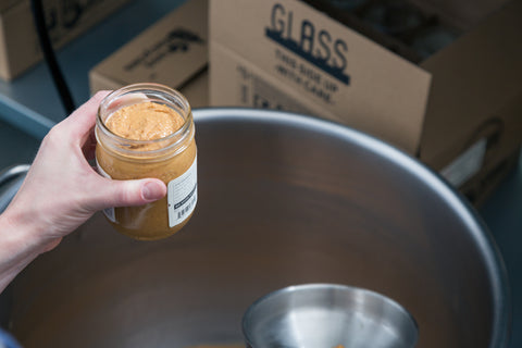 A person holds a jar of nut butter after manually filling it using a funnel.  