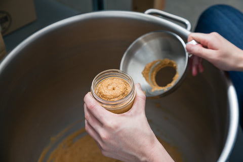 A person fills a nut butter jar using a funnel.