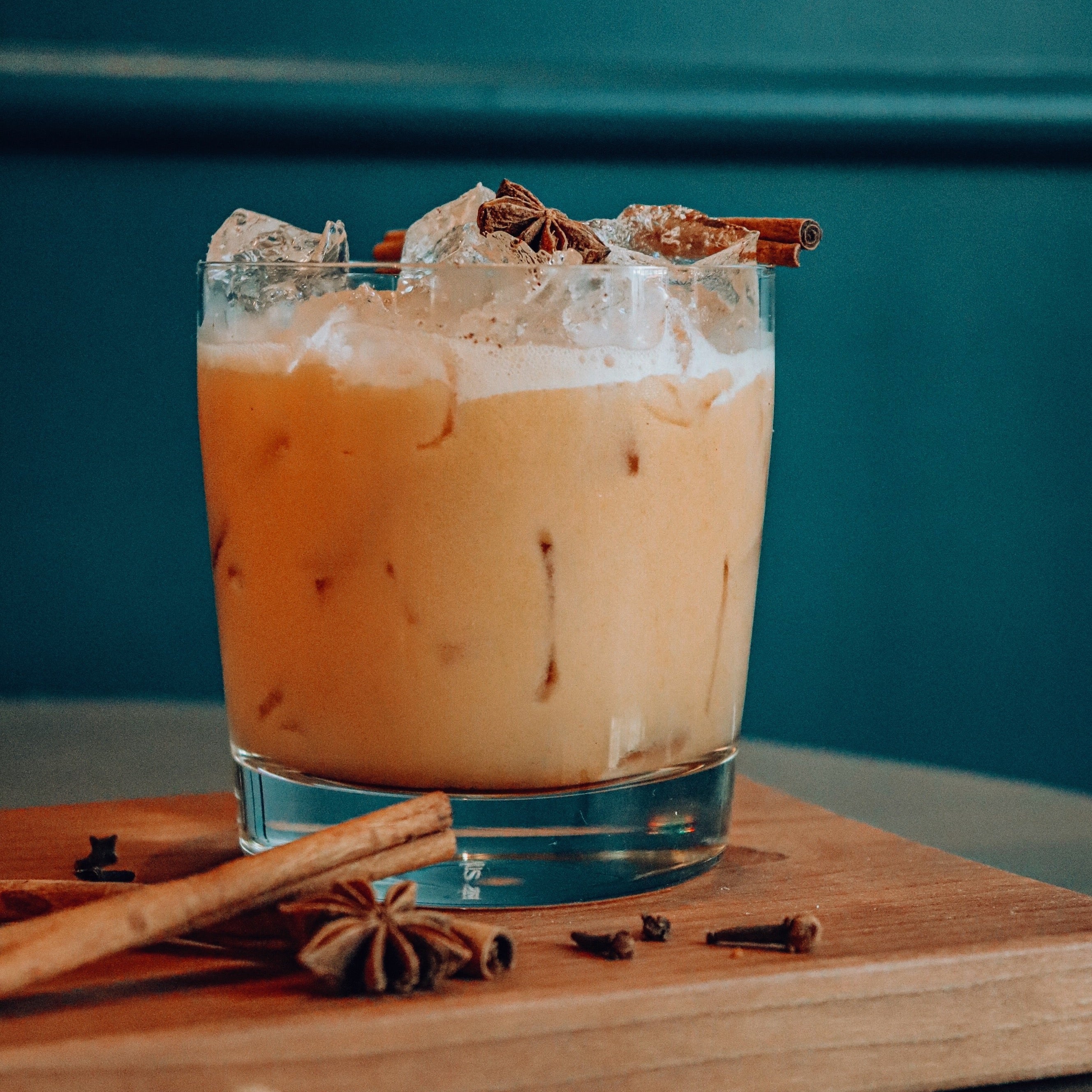 A cocktail glass holding a banana peanut butter cocktail garnished with cinnamon and anise against a teal background.