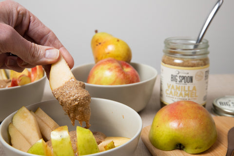 A person pulls an apple slice with Vanilla Caramel Almond & Cashew Butter out of a bowl. 
