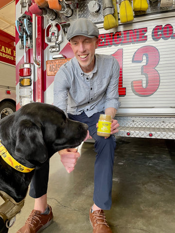 Big Spoon Roasters Co-Founder & President Mark Overbay feeds Cosmo Banana Flax Wag Butter – Peanut Butter for dogs. Mark sits on the back of the Station 13 firetruck at the Durham Fire Department.