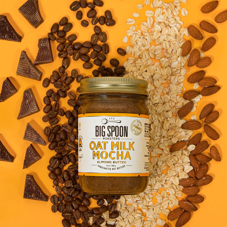 13 oz glass jar of Oat Milk Mocha nut butter with almonds, cashews, coffee beans, and chocolate spread out on a yellow/orange background