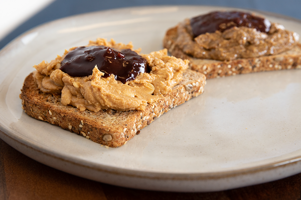 A close-up of two pieces of toast piled high with nut butter and jam on a white plate. 