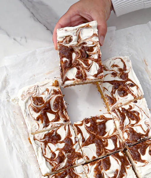 Parchment paper on a white marble background holds a no-bake cheesecake with Chocolate Sea Salt Almond Butter swirl topping.