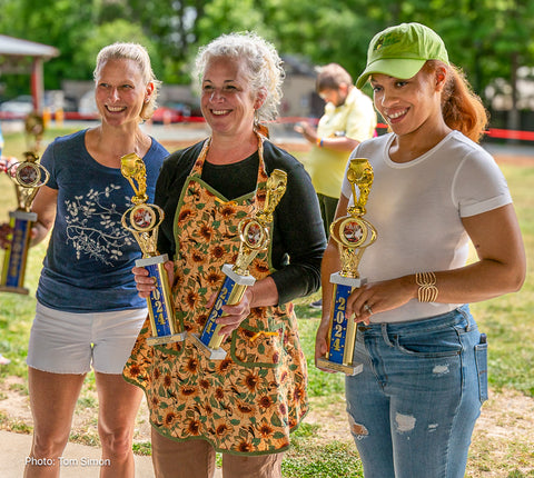 Three women stand outside holding trophies