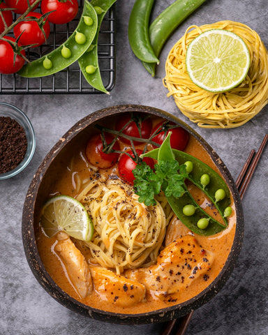lum lum noodle dish in a bowl with noodles, lime, peas and tomatoes surrounding it