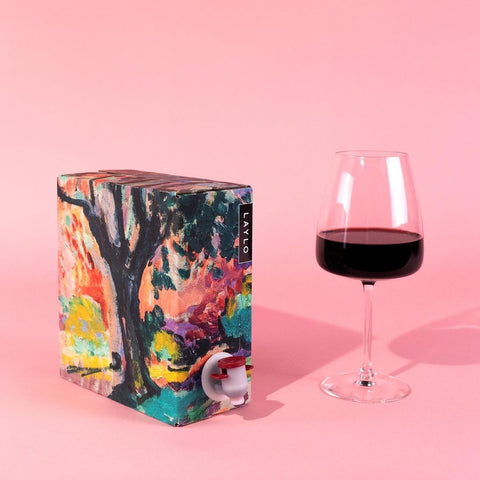 box of laylo wine next to glass filled with merlot on pink backgroound