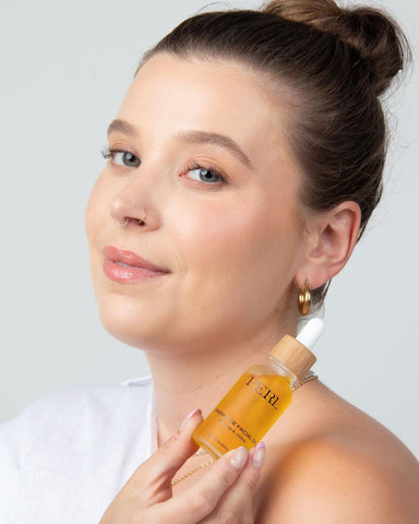girl against grey background looking to camera holding perl cosmetics facial oil