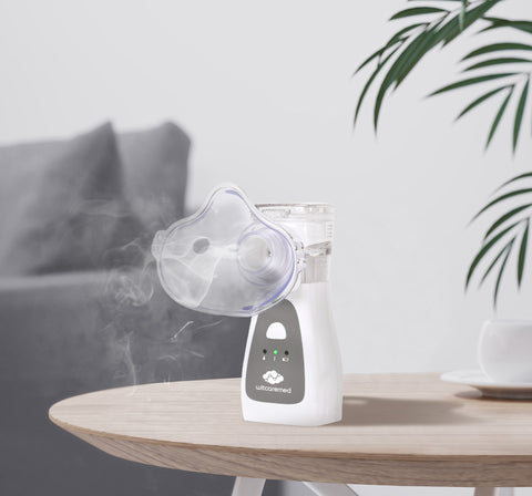 A white and gray home nebulizer sits on a table, misting medication into the air