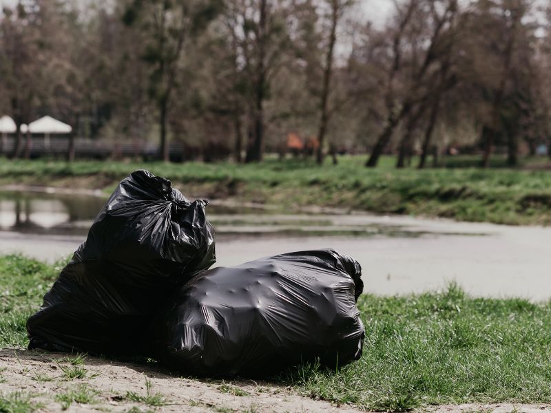 Two black garbage bags on the grass by a river