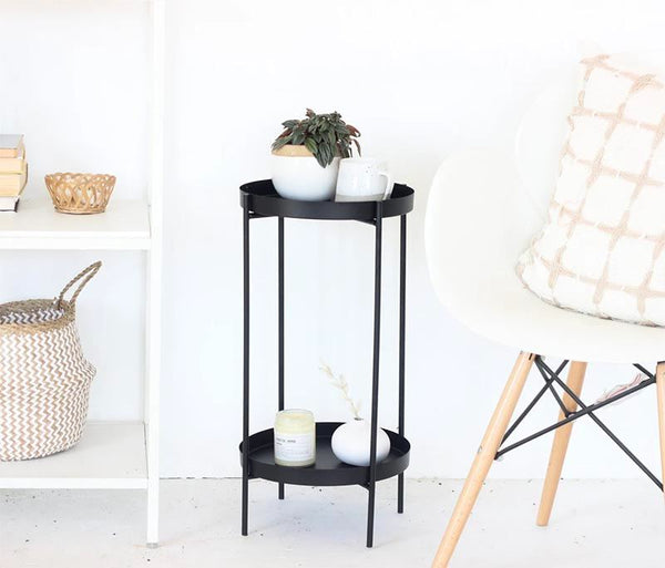 A small black table with a plant and a mug on top