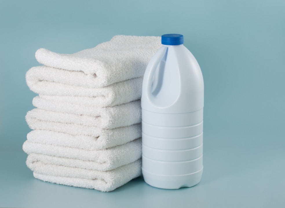A plain white bottle of bleach beside a stack of towels