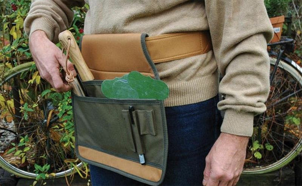 A man wearing a green and tan canvas tool belt filled with garden tools