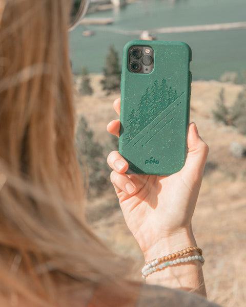 person holding up a dark green phone case with engraved pine trees