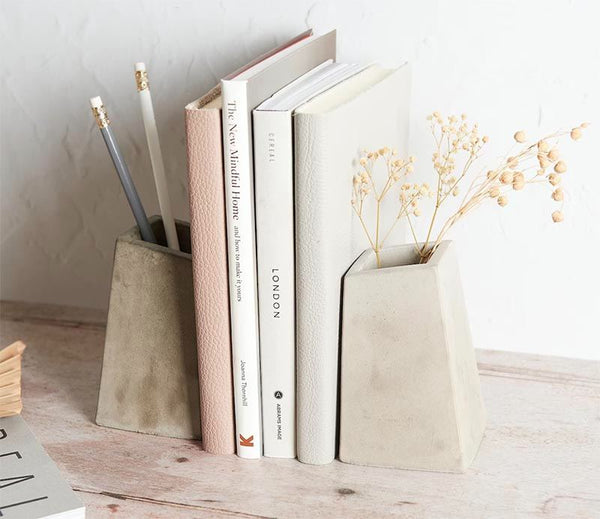 Two light gray concrete pots holding up four books