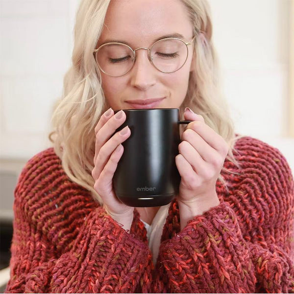 A woman drinking from a black mug