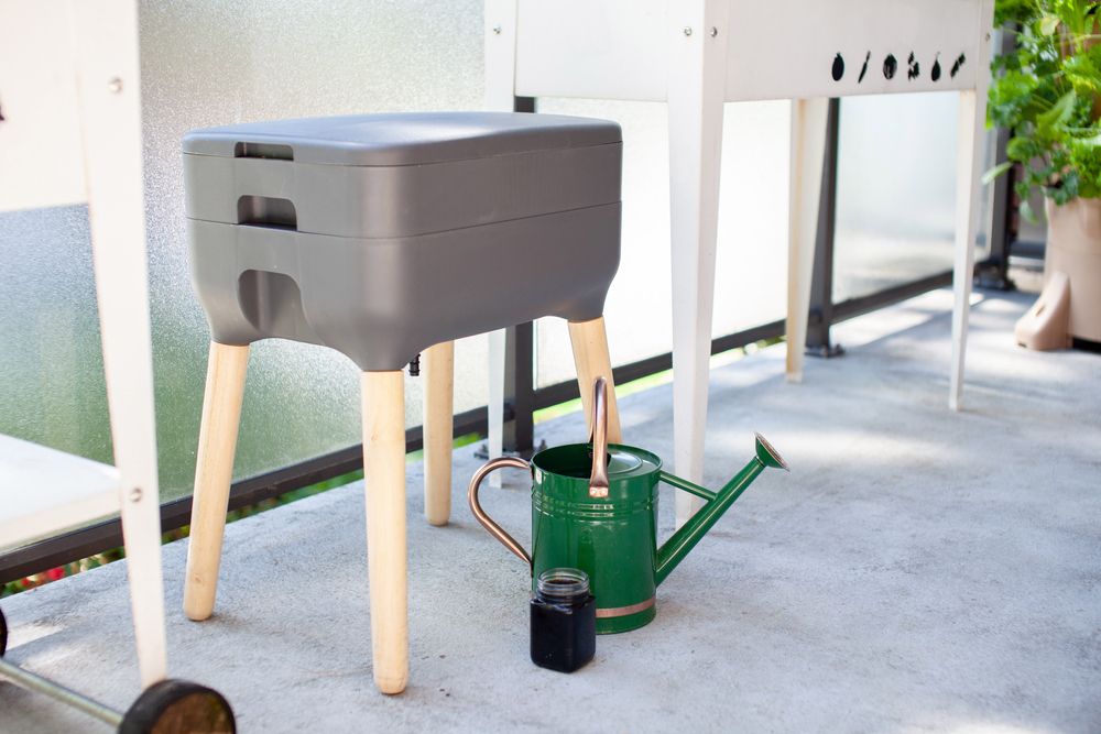 An indoor gray vermicomposting bin and watering can