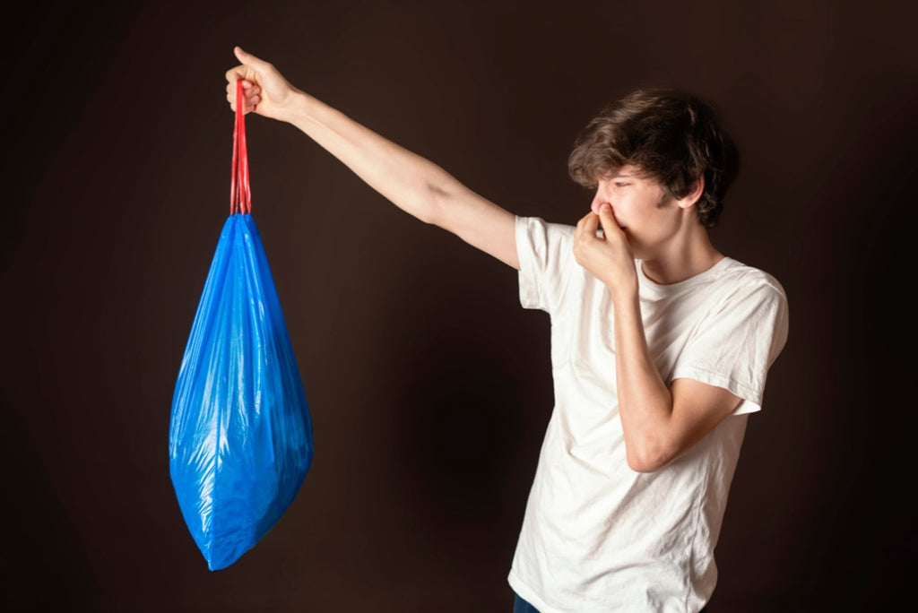 A young man holding a bad smelling blue garbage bag
