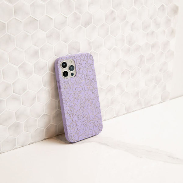 purple phone case with white flowers painted on it leaning against a wall