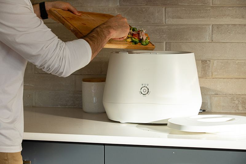 A man scraping veggie scraps into a lomi composter