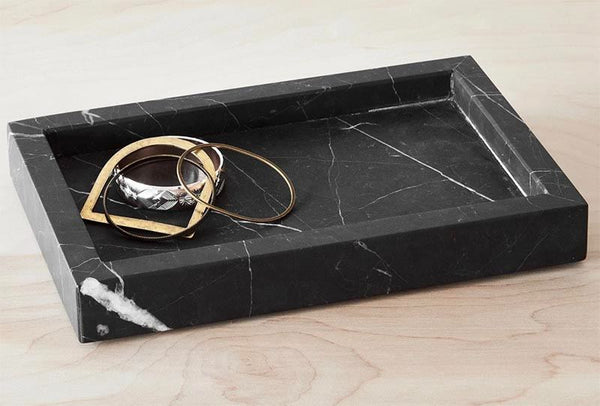 A black and white marble tray with jewelry inside