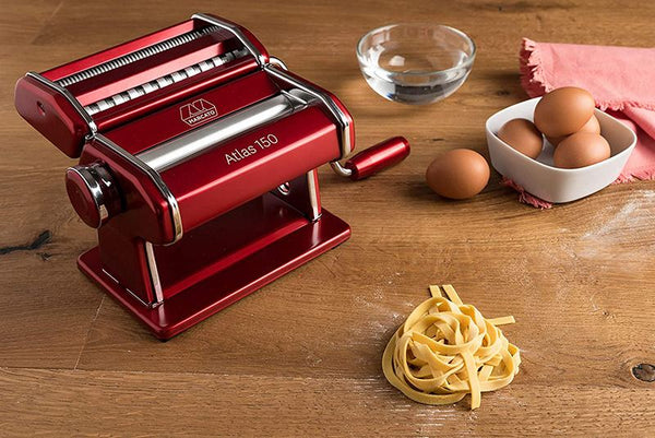 A red and silver pasta machine on a wooden background