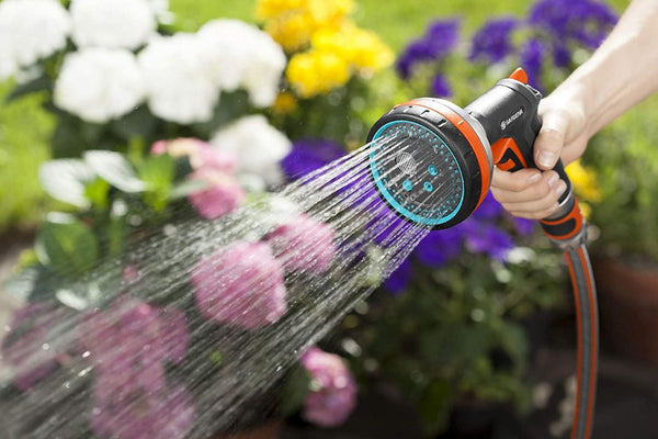 A hand holding a spray nozzle watering flowers