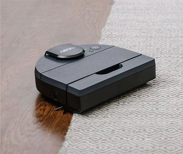 A black robot vacuum on a wood and carpeted floor
