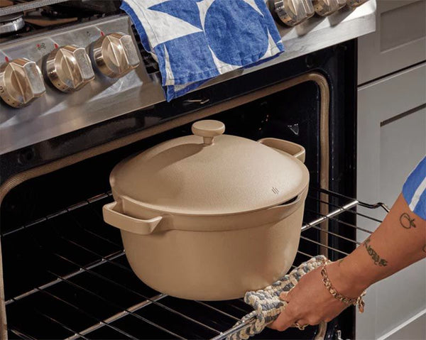 An off-white pot with a lid being placed into an open oven