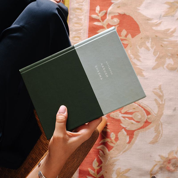 A hand holding a two-toned notebook with a name printed on it