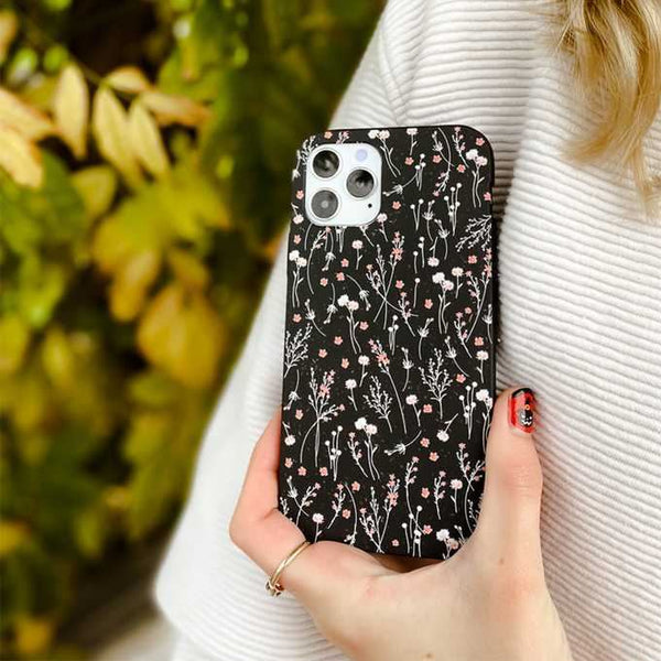 person holding a black phone case with flowers on it next to their shoulder