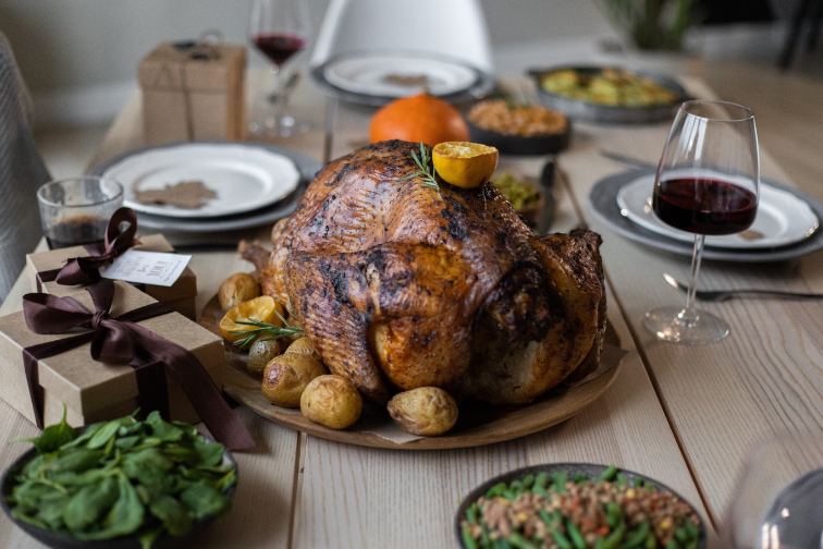 A holiday roast turkey on a dining table surrounded by food and gifts