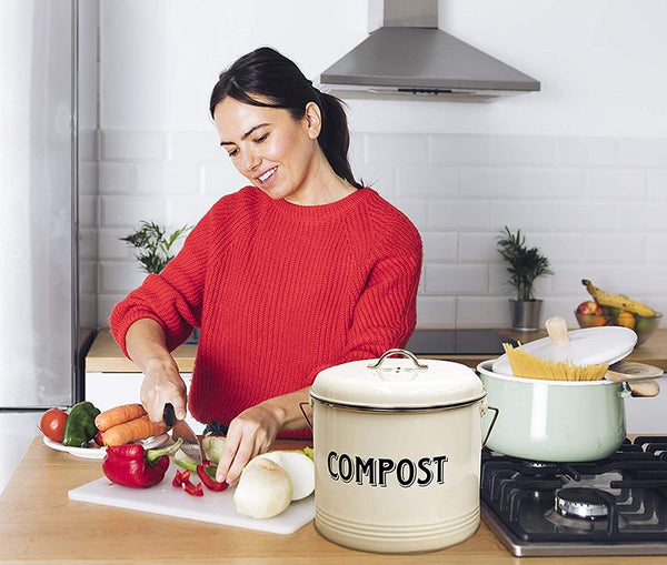 A woman smiling while cutting veggies next to a cream colored compost bin