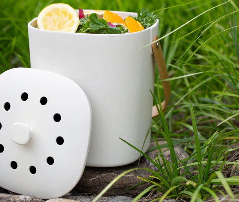 White compost bin with wood handle sitting in the grass