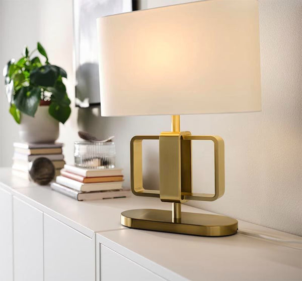 A lamp with a white shade and a brass base sitting on a console table