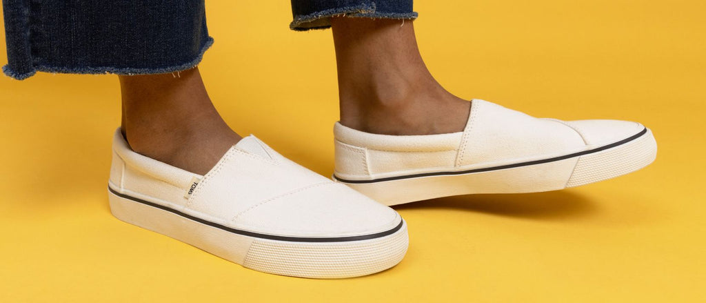 A woman posing in white Toms shoes