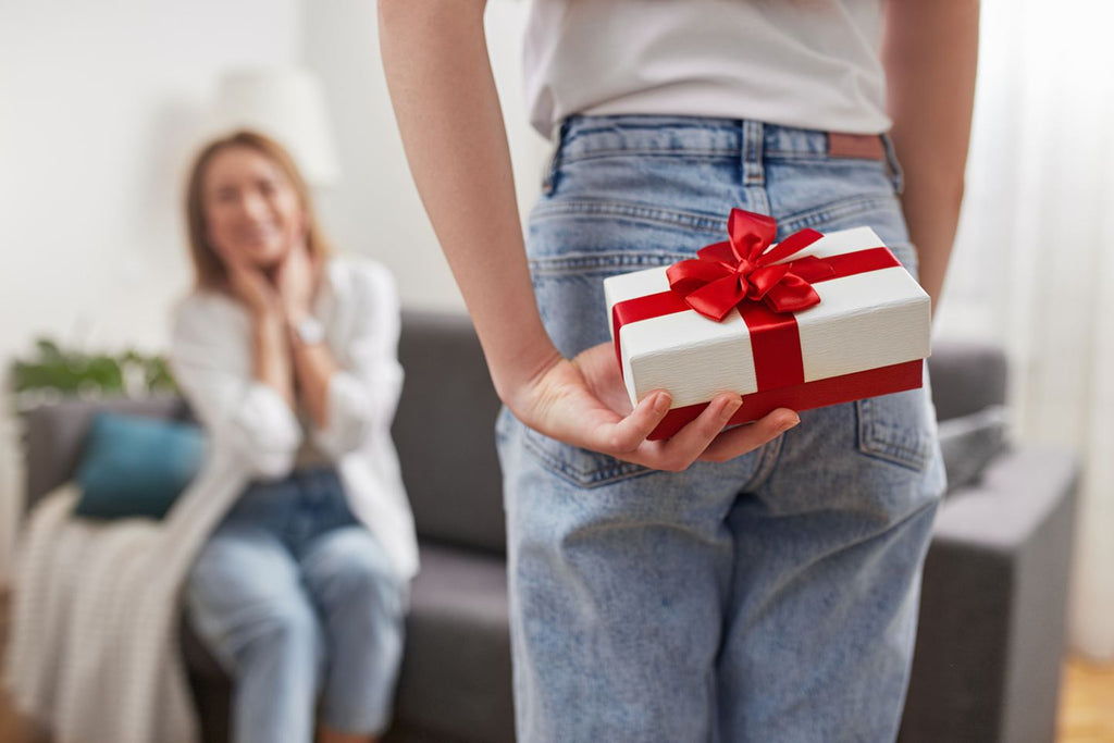 Someone holding a wrapped gift behind their back with a smiling woman in the background