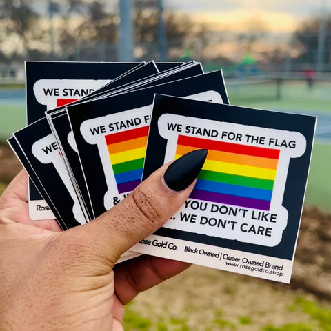 hand full of rainbow pride stickers that say we stand for the flag and if you don't like it we don't care