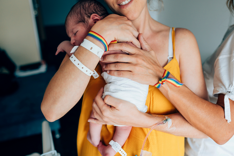 lesbian moms with rainbow ribbons holding their newborn baby
