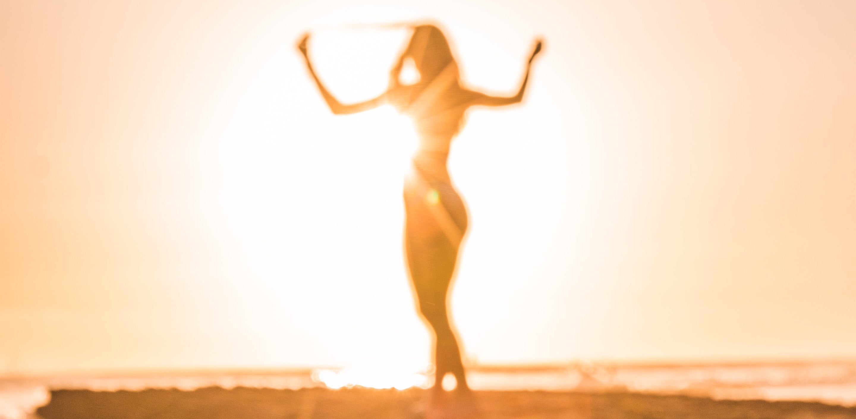 silhouette of a slender woman raising her arms in front of the sun