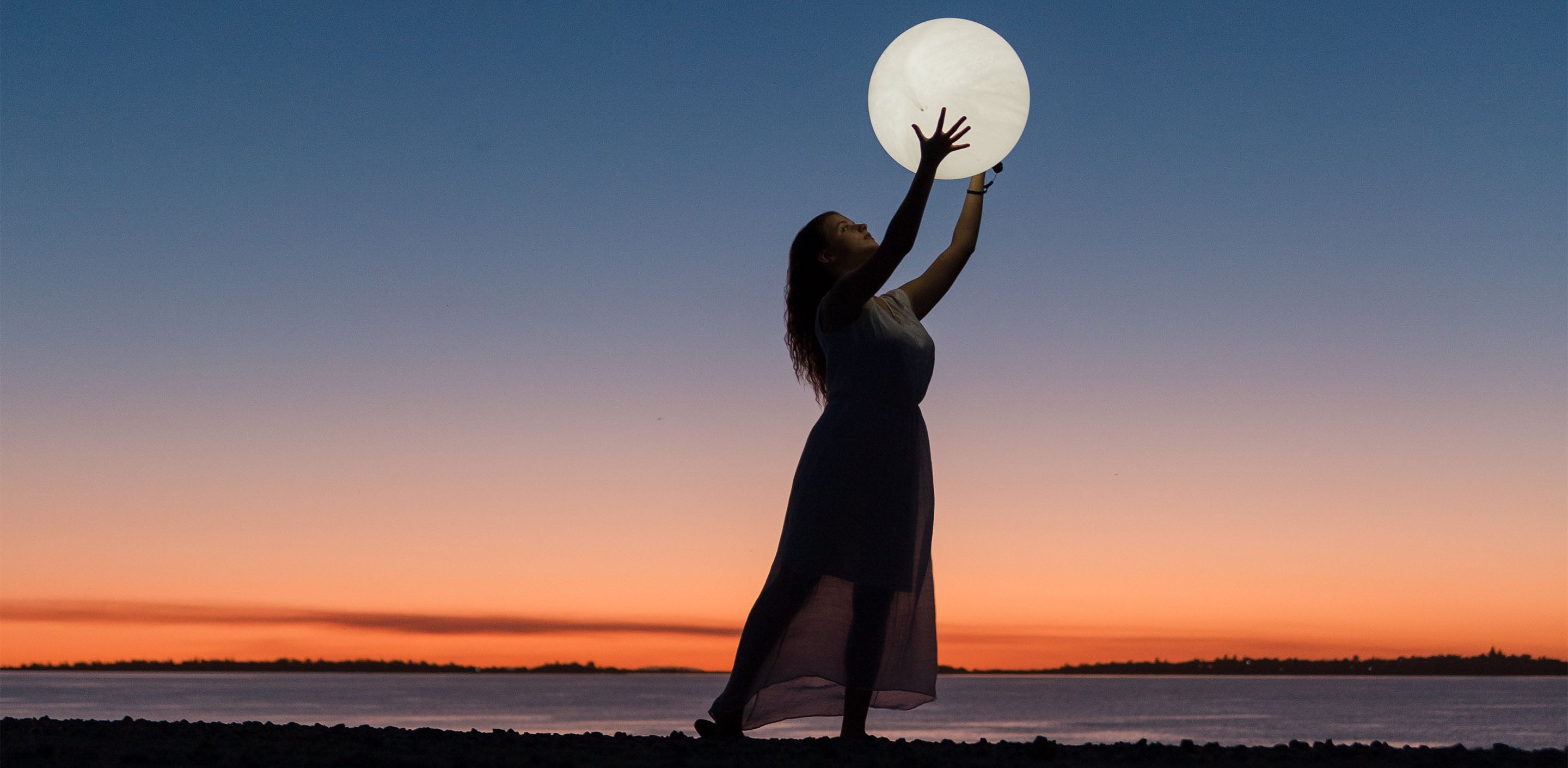 silhouette of a woman catching the moon in her hands in front of the sunset