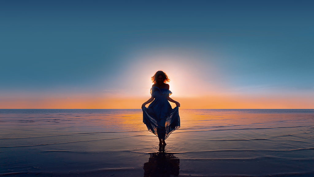 Mujer bohemia caminando en el océano con una hermosa puesta de sol
