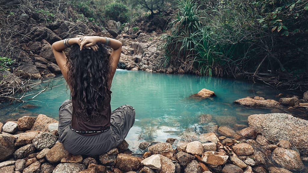 Mujer bohemia en la naturaleza sentada junto a un río